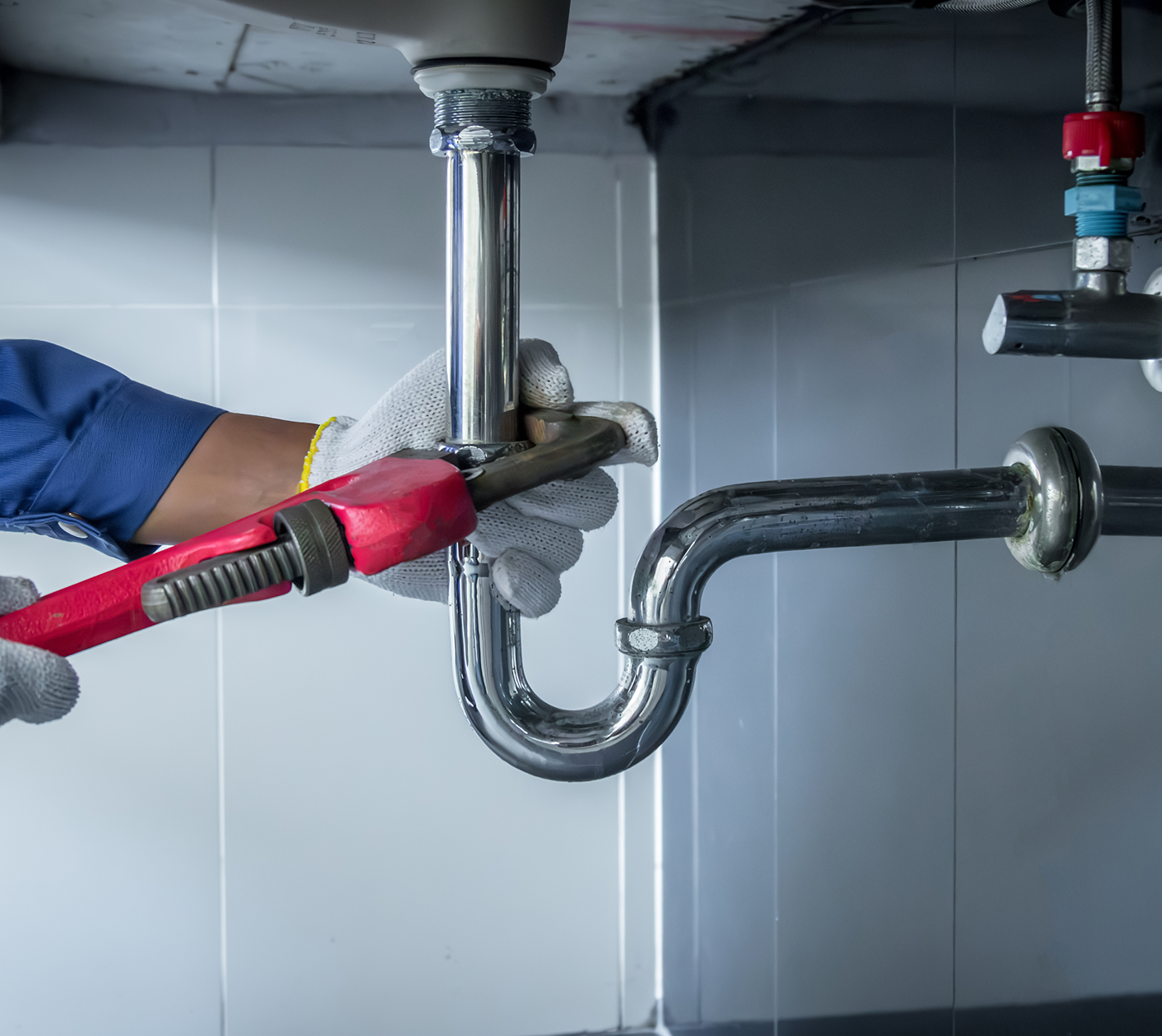 Plumber fixing pipe with wrench under sink.